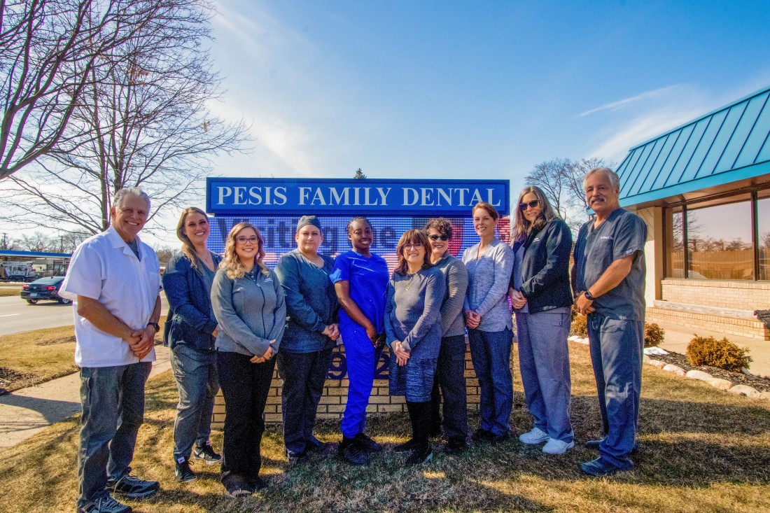  The team at Pesis Dental Group standing in front of the clinic's sign